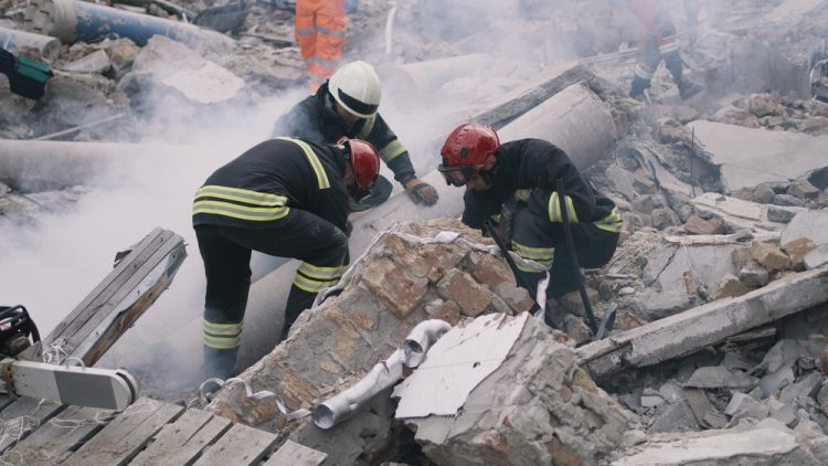 Men in protective uniforms and hardhats removing pieces of broken building during rescue mission after earthquake