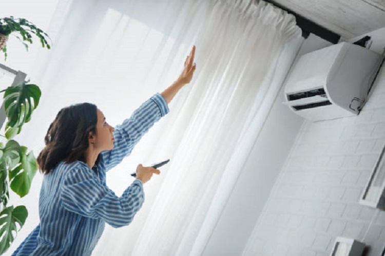 Woman is checking to see if the air conditioner is cooling. She is holding the remote to the air conditioner and raised her hand to check temperature.